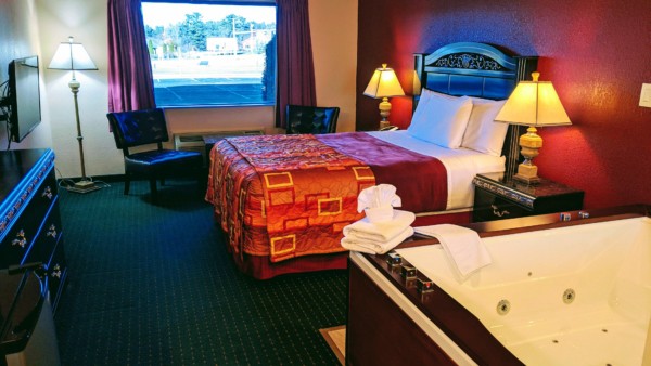Deluxe Whirlpool Suite at Grand Marquis Hotel in Wisconsin Dells - front view of whirlpool, bed, TV, 2 chairs, and partial views of mini fridge, dressers, and table